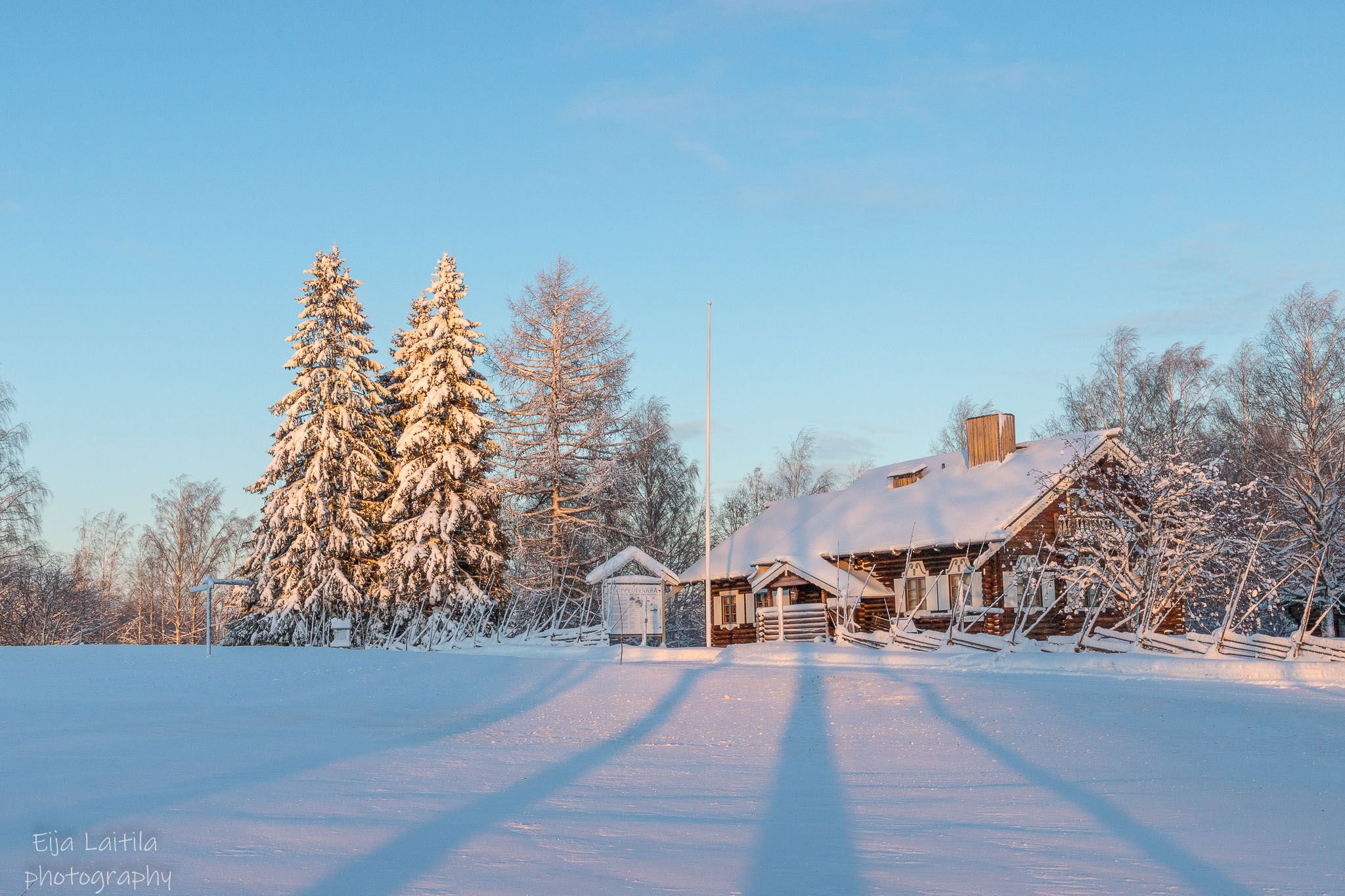 Lumisen pellon takana kuurainen metsä ja punainen talo.