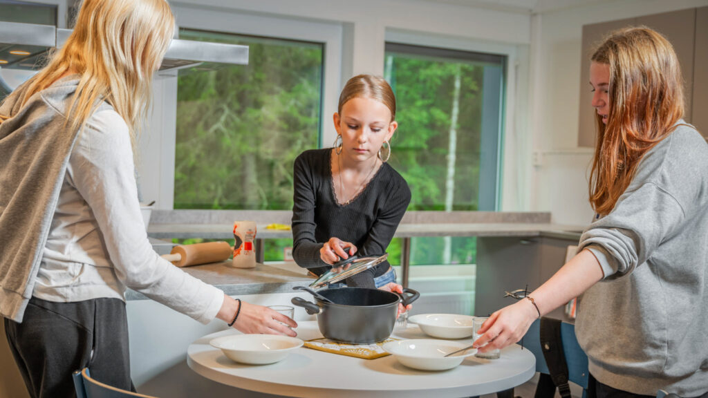 Kolme tyttöä työskentelevät kotitalousluokassa. 